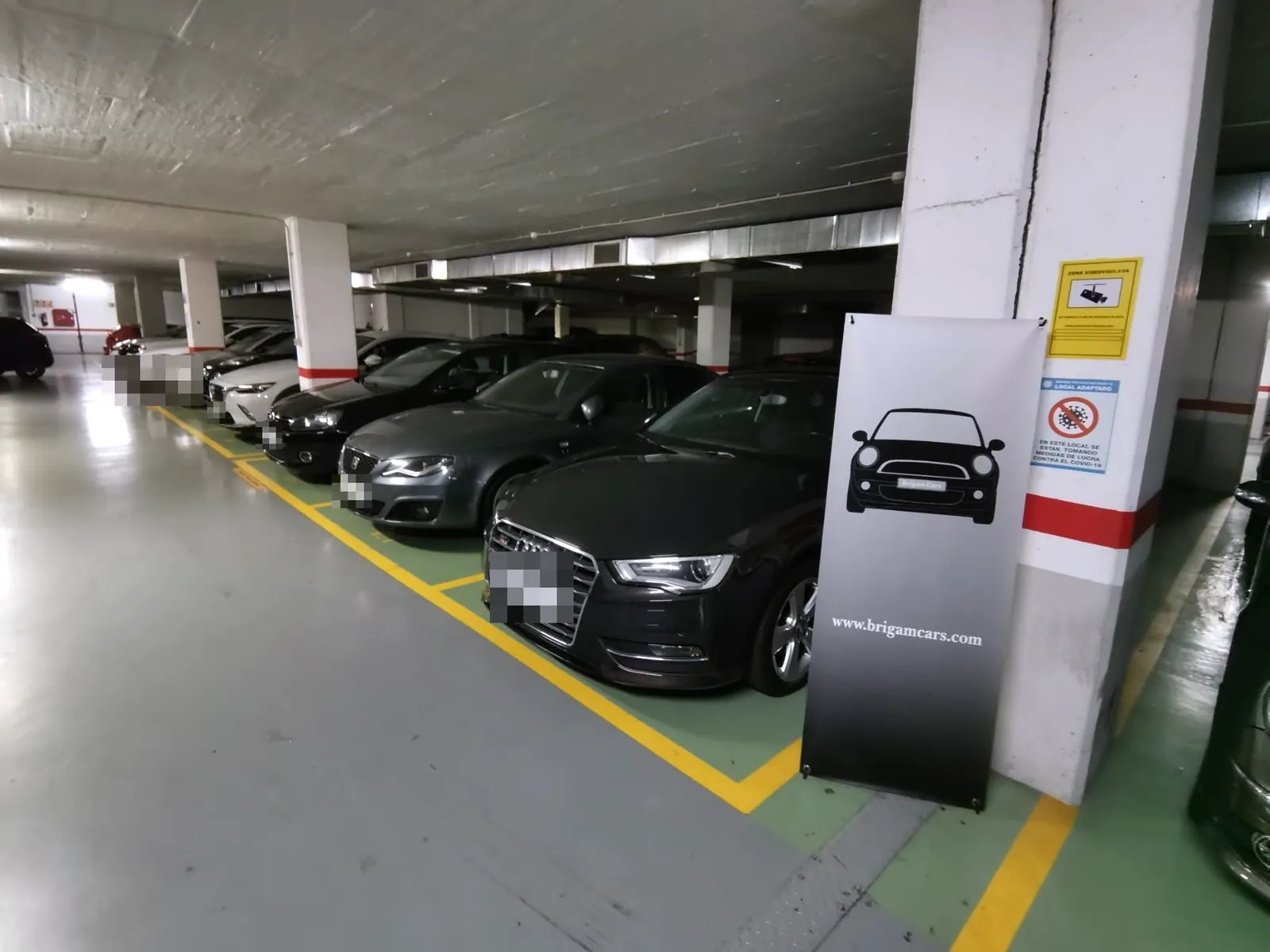 Fila de coches en el almacén de Brigam Cars, con un Audi negro en primer plano junto al cartel enrollable de la marca.