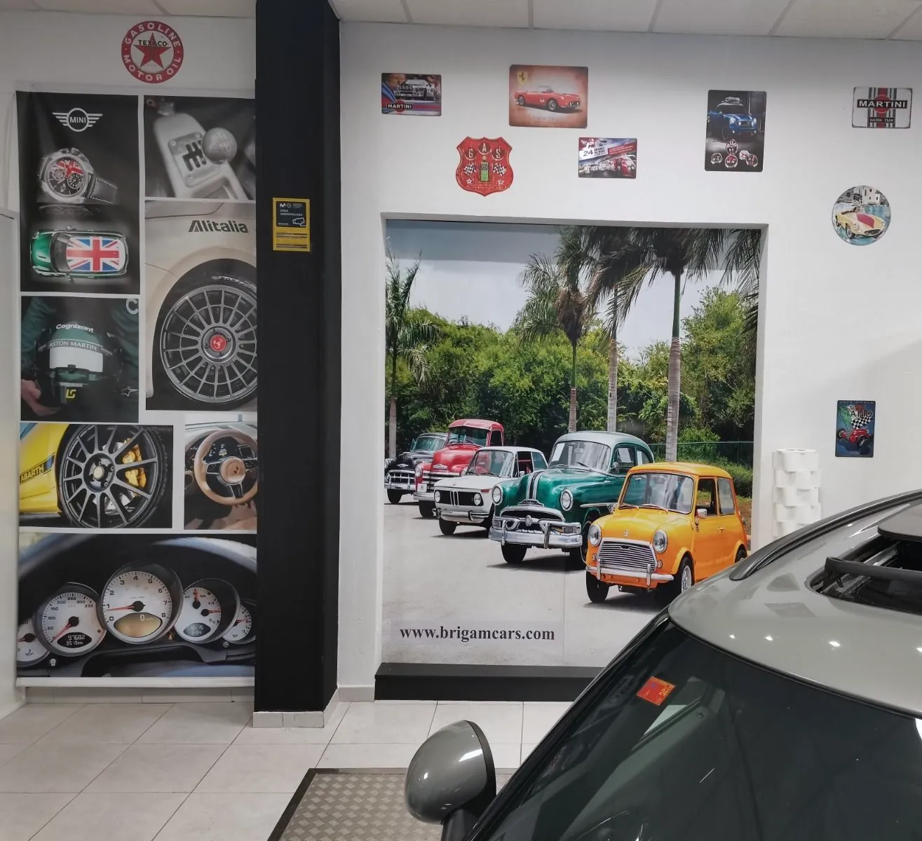 Pared del local de Brigam Cars con un fotomural de coches clásicos, placas decorativas de motor y la dirección www.brigamcars.com.
